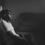 black and white image of man sitting down in dimly lit room