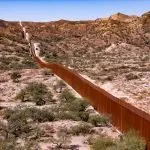 A long metal fence in the middle of a desert