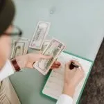 A person counting cash and filling in a weekly budget planner